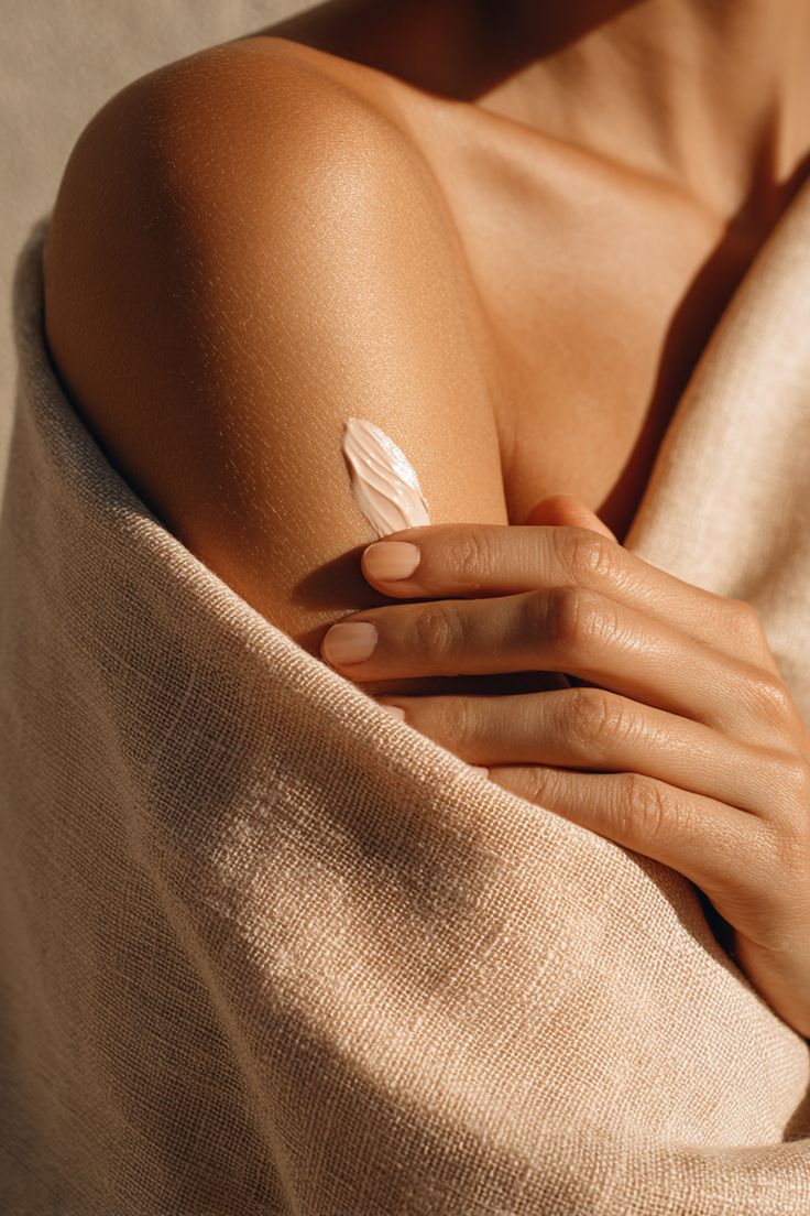 Detalle de piel hidratada con crema sobre textil natural, evocando cuidado personal y bienestar
